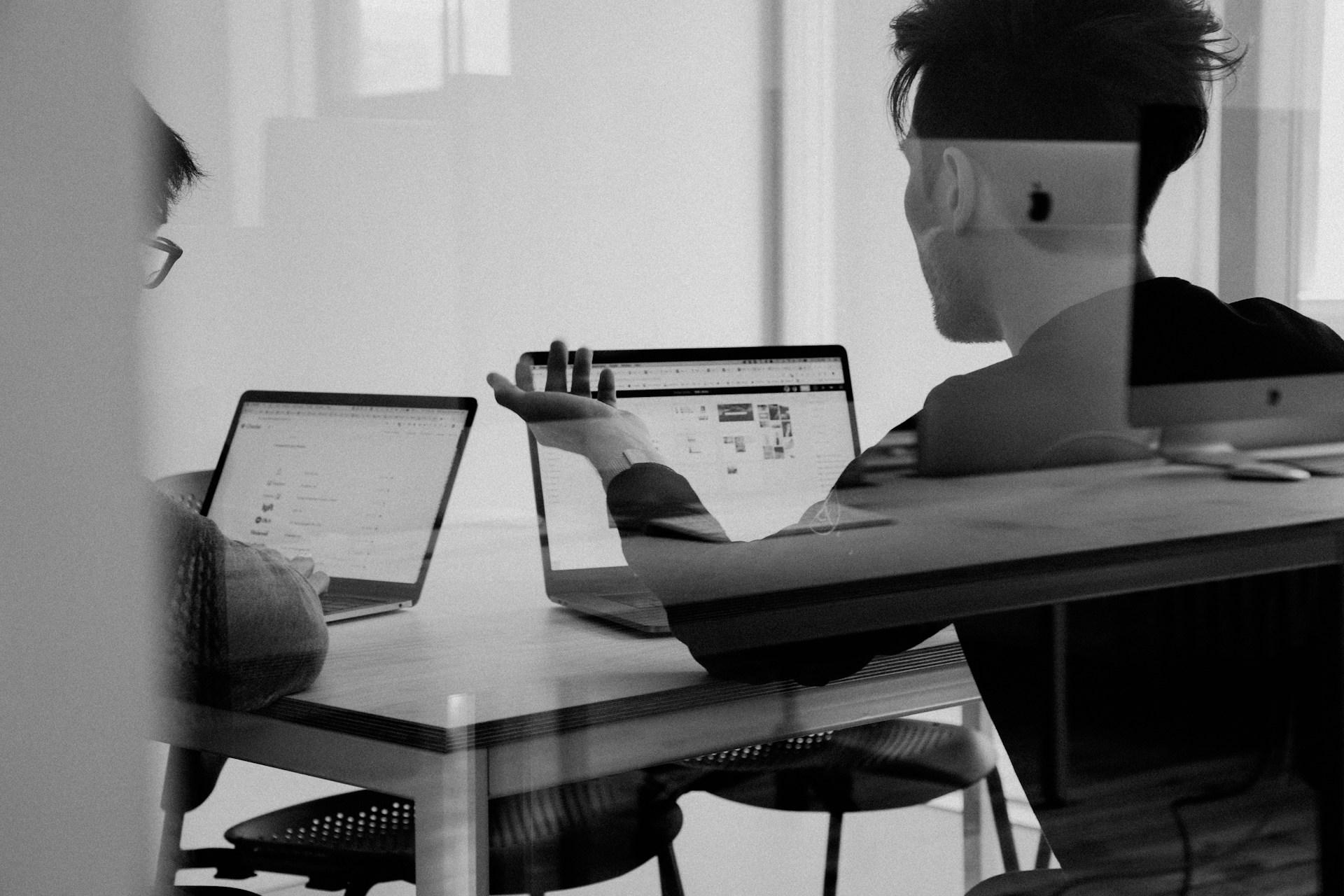 Zwei Entwickler sitzen mit Laptops an einem Konferenztisch